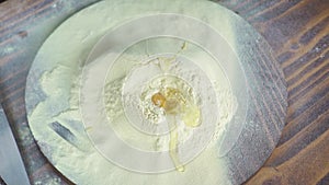 Fresh eggs falling on flour on wooden table top view. Slow motion broken chicken egg in flour powder for dough preparing