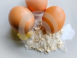 Fresh eggs seen with flour and a knob of butter in a mixing bowl.
