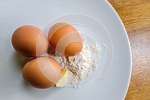 Fresh eggs seen with flour and a knob of butter in a mixing bowl.