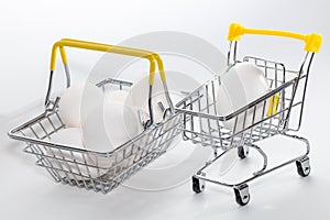 Fresh eggs in a shopping cart and a basket next to it. Shopping, purchasing, and food delivery concept