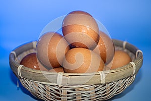 Fresh eggs with water condensation in a rattan basket. Isolated on blue background. Shallow depth of field
