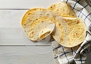 Fresh, empty wheat tortilla flat lay top view on dishcloth on white wooden table