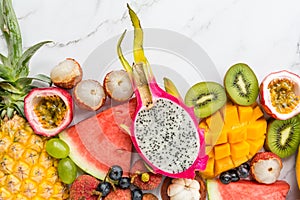 Fresh exotic fruits and tropical palm leaves on white marble background - papaya, mango, pineapple, passion fruit