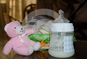 Fresh expresed breast milk in baby bottle, pink teddy bear and frozen breast milk in storage bags in background