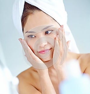 Fresh-faced beauty. An attactive young Asian woman applying moisturizer with a towel on her head.