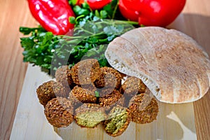 Fresh falafel balls, pita bread and red pepper on a wooden cutting board
