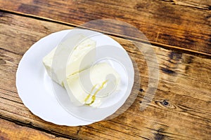 Fresh farm piece of butter on a white plate on wooden background Farm products Plate on the left at photo