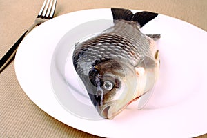 Fresh fish carp on a white plate with fork