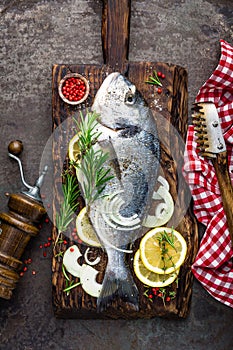 Fresh fish dorado with ingredients for cooking on wooden board. Raw sea bream or dorada fish on dark vintage metal background. Die