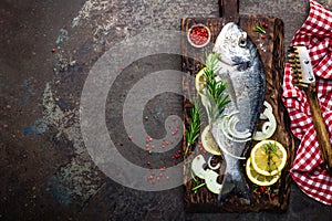 Fresh fish dorado with ingredients for cooking on wooden board. Raw sea bream or dorada fish on dark vintage metal background. Die