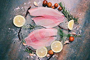 Fresh fish fillet sliced for steak or salad with herbs spices rosemary tomato and lemon - Raw tilapia fillet fish and salt on dark