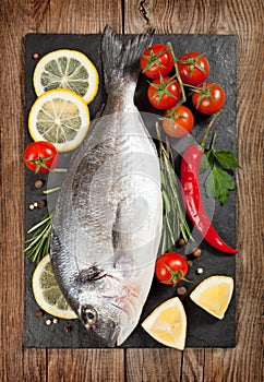 Fresh fish, lemon, spices and cherry tomatoes on a stone board