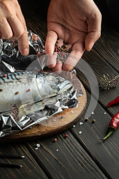 Fresh fish must be wrapped in foil and aromatic spices and peppers must be added. Close-up of chef hands while preparing delicious