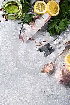 Fresh fish. Sea Bass raw with salt, pepper, parsley, olive oil and lemon on cutting board on light gray concrete rustic background