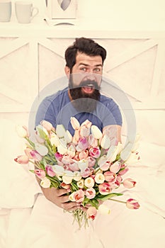 Fresh flowers. Bearded hipster in bed. Spring in bedroom. Man hold tulips bouquet while relaxing in bed. Flowers