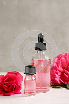 Fresh flowers and bottles of rose essential oil on table