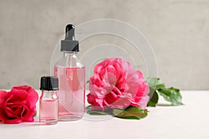 Fresh flowers and bottles of rose essential oil on table