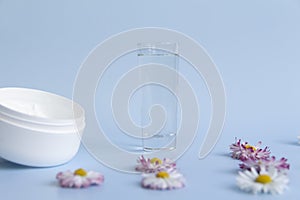 Fresh flowers, daisies are laid out in a corner, with a glass of clean water and a white jar with a cream cosmetic on a blue