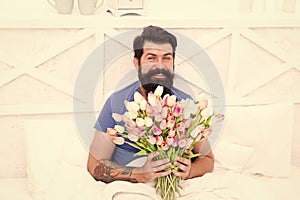 Fresh flowers surprise. Gift for spouse. Bearded hipster in bed. Spring mood in his bedroom. Man hold tulips bouquet