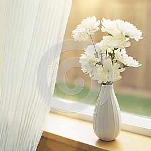 Fresh flowers in vase on windowsill with sheer fabric curtains window coverings. Simple, natural, home interior decor. photo