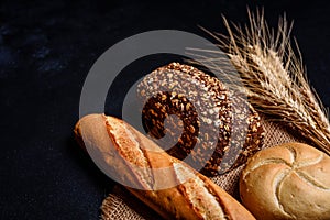 Fresh fragrant bread with grains and cones of wheat against a dark background