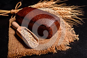 Fresh fragrant bread with grains and cones of wheat against a dark background