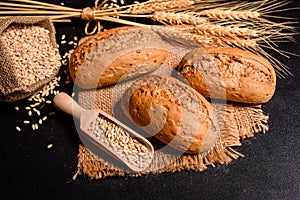 Fresh fragrant bread with grains and cones of wheat against a dark background