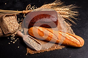Fresh fragrant bread with grains and cones of wheat against a dark background