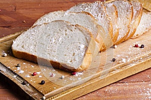 Fresh and fragrant white bread is sliced and lying on a wooden b
