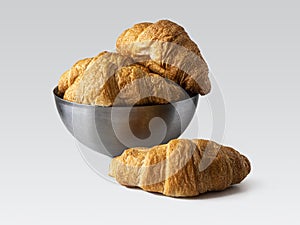 Fresh French croissants in a metal hemispherical bowl on a light background
