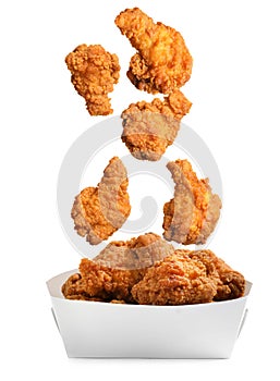 Fresh fried chicken falling into container on white background photo