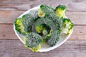 Fresh frozen broccoli on white plate, wooden table, healthy diet food