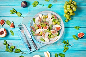 Fresh fruit and berry salad with grapes, fig and peach on blue wooden background. Healthy food.