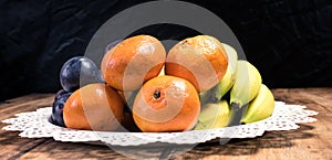 Fresh fruit (orange, plum, banana, kiwi) in the basket on a vintage wooden table