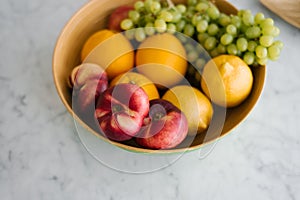 Fresh fruit, peaches, grapes and oranges in a plate on the marble table in the kitchen. Healthy and wholesome food