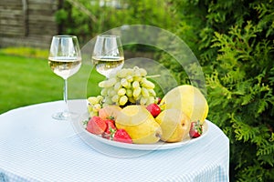 Fresh fruit on a plate and wineglass with white wine on a table in the garden