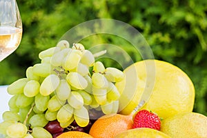 Fresh fruit on a plate and wineglass with white wine on a table in the garden