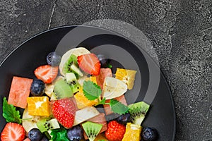 Fresh fruit salad on black plate. Top view