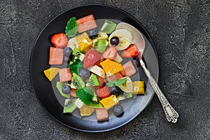 Fresh fruit salad on black plate. Top view