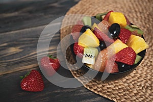 Fresh fruit salad, top view in a bowl on wooden background, vegetarian food concept