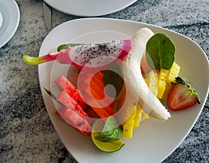 Fresh fruit served on a white dish on a marble table with dragonfruit