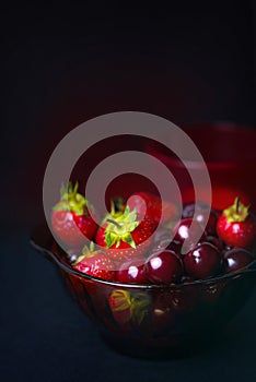 Fresh fruit of strawberries and cherries in a glass dark Cup