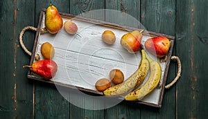 Fresh fruit on a white wooden tray: banatas, pears, apricots. Countryside setting. Top view.