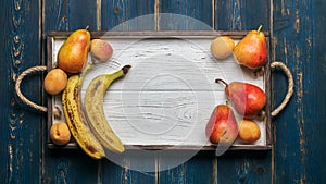 Fresh fruit on a white wooden tray: banatas, pears, apricots. Countryside setting. Top view.