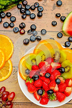 Fresh fruits concept, Tropical fruits and assorted berry salad in bowl on wooden background