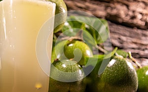 Fresh fruits and glass of passion fruit Passiflora edulis juice amid green leaves and wooden background