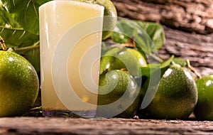 Fresh fruits and glass of passion fruit Passiflora edulis juice amid green leaves and wooden background photo