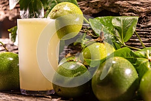 Fresh fruits and glass of passion fruit Passiflora edulis juice amid green leaves and wooden background photo
