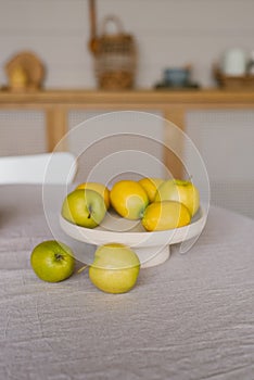 Fresh fruits lemons and green apples are on a white plate on the kitchen table