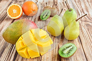 Fresh fruits of mango and mango cubes, pears, orange, kiwis on wooden background